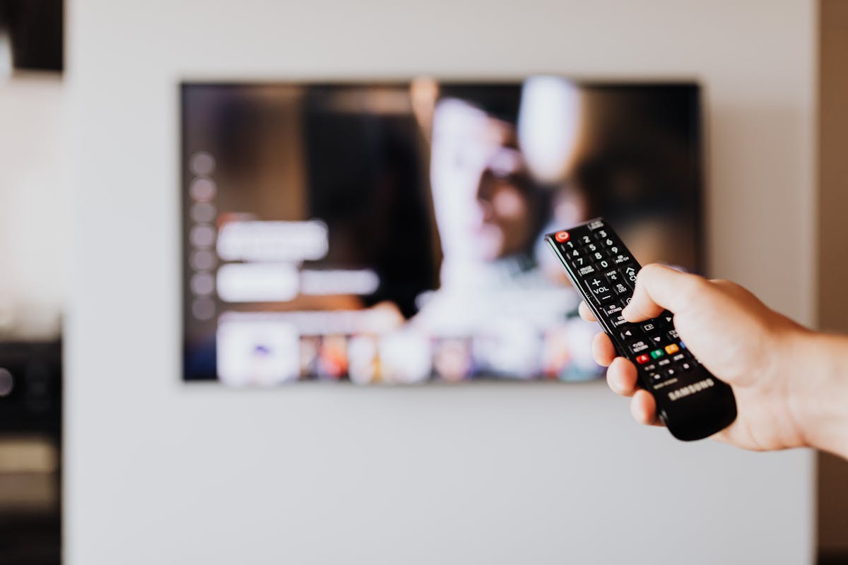 Primer plano de una mano usando un mando a distancia frente al televisor encendido